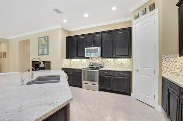 Kitchen featuring visible vents, appliances with stainless steel finishes, a sink, light stone countertops, and dark cabinetry