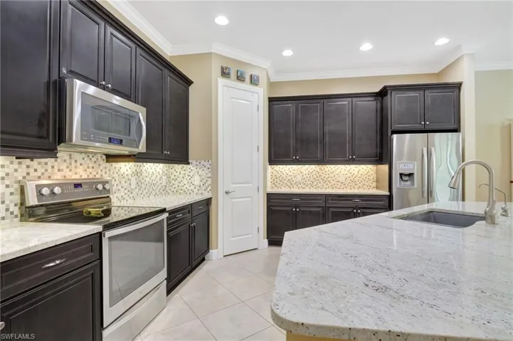 Kitchen with light tile patterned floors, ornamental molding, light stone countertops, stainless steel appliances, and a sink