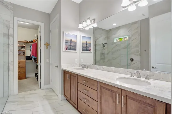 Full bath with marble finish floor, a sink, a spacious closet, and walk in shower