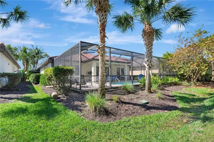 Back of property with a lanai, an outdoor pool, and a lawn