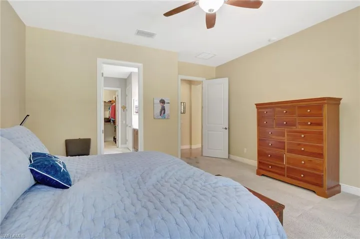 Bedroom with light colored carpet, a ceiling fan, baseboards, visible vents, and a walk in closet