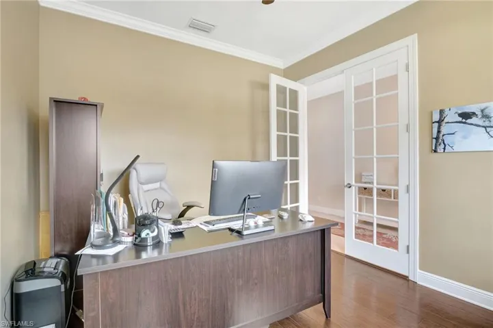 Office space with baseboards, visible vents, dark wood-type flooring, crown molding, and french doors