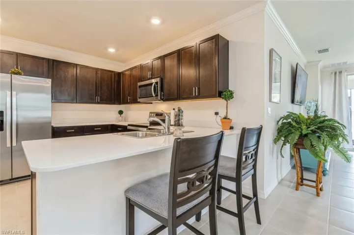Kitchen featuring dark brown cabinetry, kitchen peninsula, appliances with stainless steel finishes, and a kitchen bar