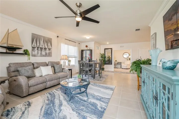 Living room featuring light tile patterned floors, ceiling fan, and crown molding
