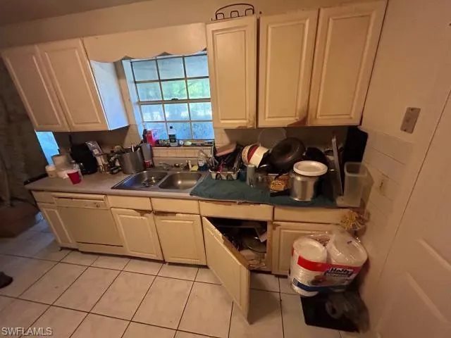Kitchen featuring decorative backsplash, white dishwasher, white cabinets, light tile patterned floors, and sink