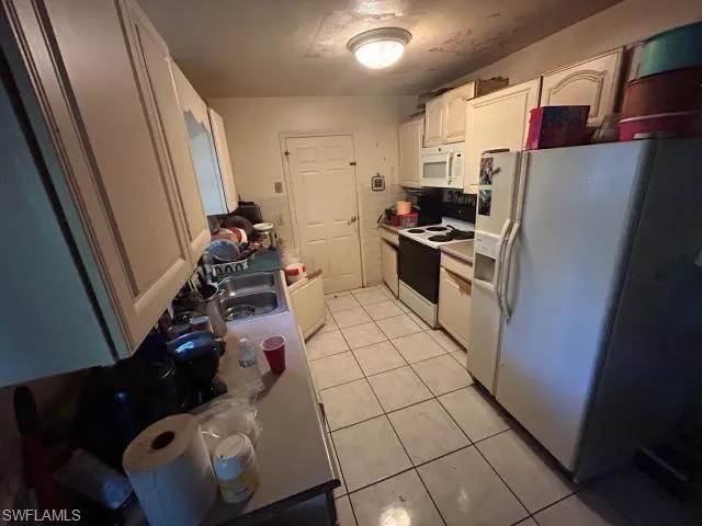 Kitchen with white cabinets, sink, white appliances, and light tile patterned floors