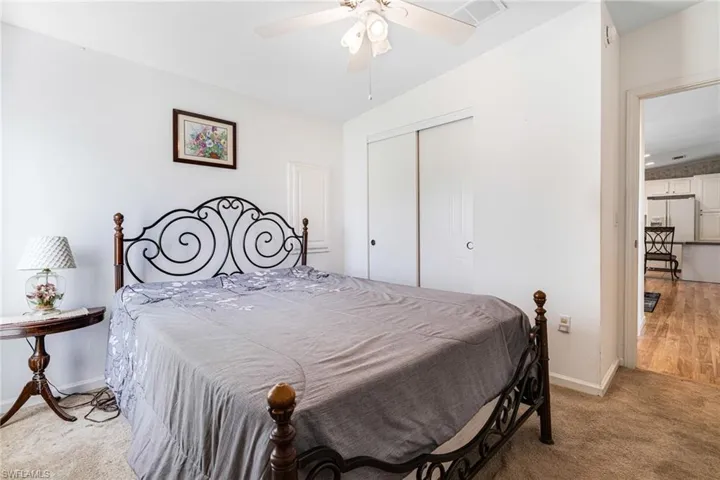 Carpeted bedroom featuring white refrigerator with ice dispenser, a closet, vaulted ceiling, and ceiling fan