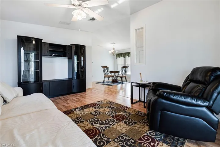 Living room with ceiling fan with notable chandelier, vaulted ceiling, and wood-type flooring