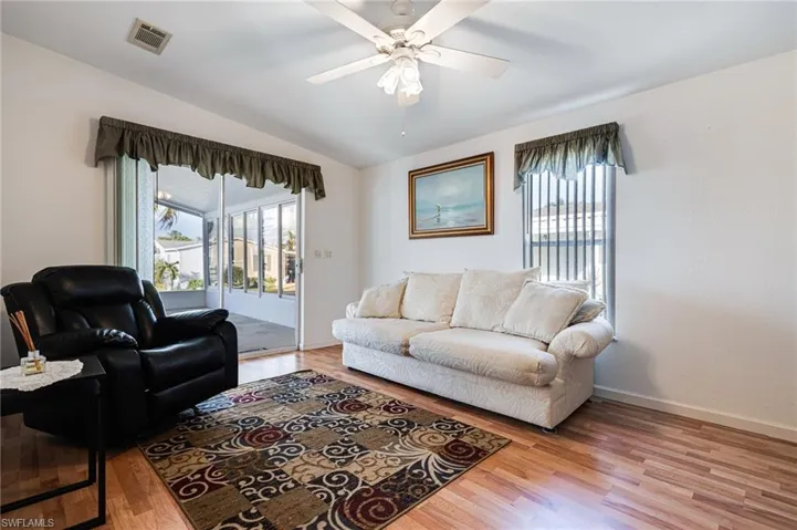 Living room with lofted ceiling, ceiling fan, and light wood-type flooring