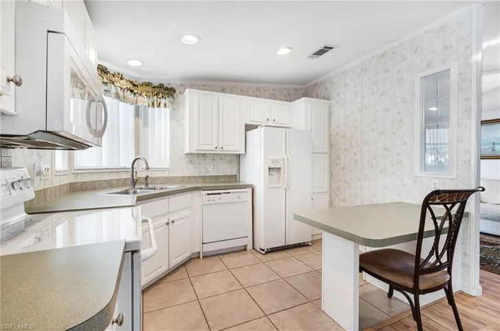 Kitchen with ornamental molding, white cabinetry, sink, vaulted ceiling, and white appliances