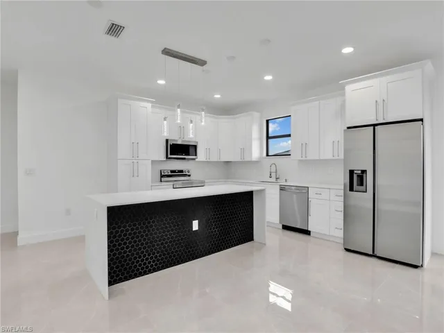 Kitchen with visible vents, a kitchen island, a sink, light countertops, and appliances with stainless steel finishes