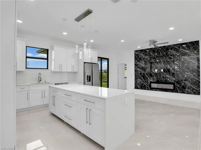 Kitchen featuring recessed lighting, stainless steel fridge with ice dispenser, a sink, light countertops, and white cabinetry