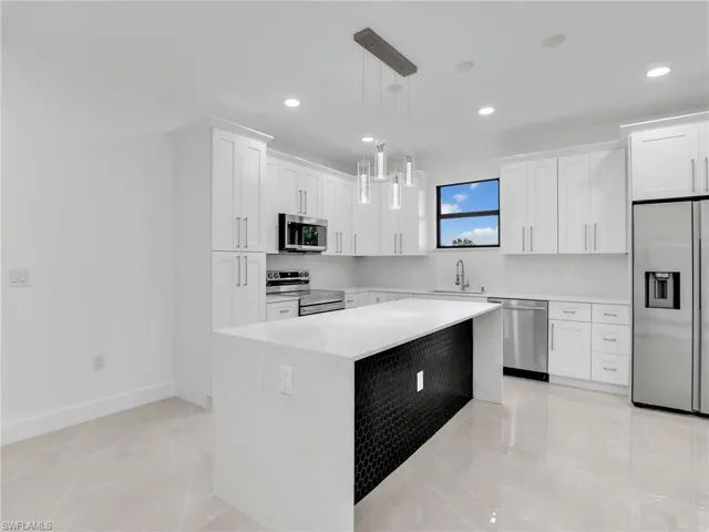 Kitchen with a kitchen island, light countertops, appliances with stainless steel finishes, white cabinetry, and a sink