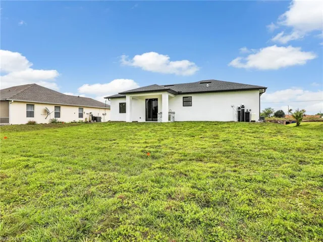 Rear view of property featuring stucco siding, a lawn, and central AC unit