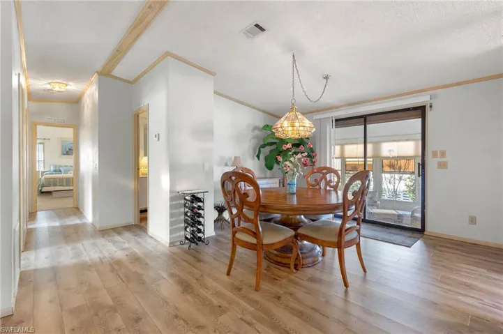 Dining room with light wood-style floors, visible vents, a textured ceiling, and ornamental molding