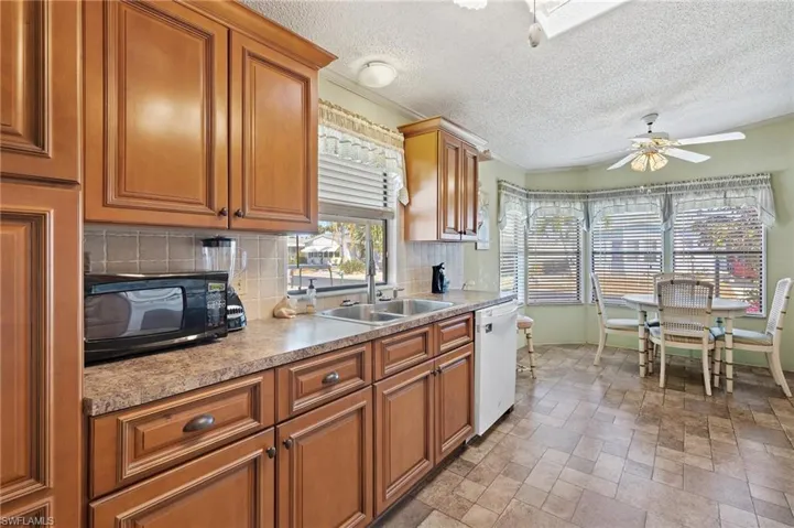 Kitchen featuring tasteful backsplash, light countertops, white dishwasher, ceiling fan, and black microwave