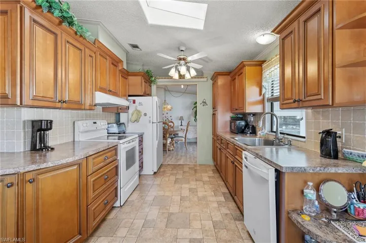 Kitchen featuring a skylight, light countertops, a sink, white appliances, and under cabinet range hood