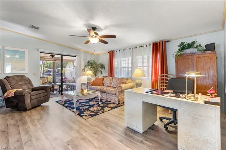 Office area with light wood finished floors, lofted ceiling, visible vents, ceiling fan, and a textured ceiling