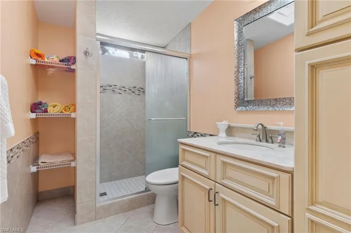 Bathroom featuring a textured ceiling, toilet, vanity, a shower stall, and tile patterned floors