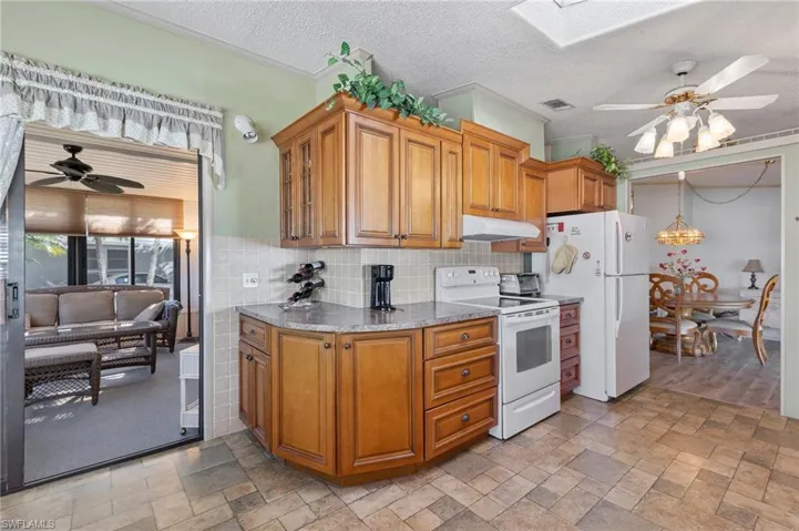 Kitchen featuring under cabinet range hood, white appliances, visible vents, brown cabinets, and glass insert cabinets