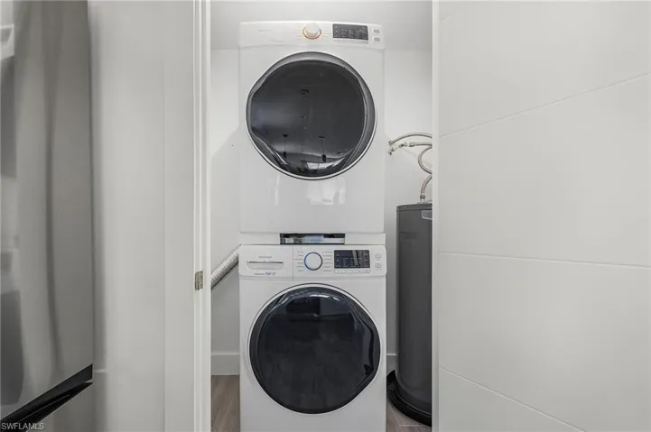 Laundry room with water heater, stacked washer / dryer, and wood finished floors