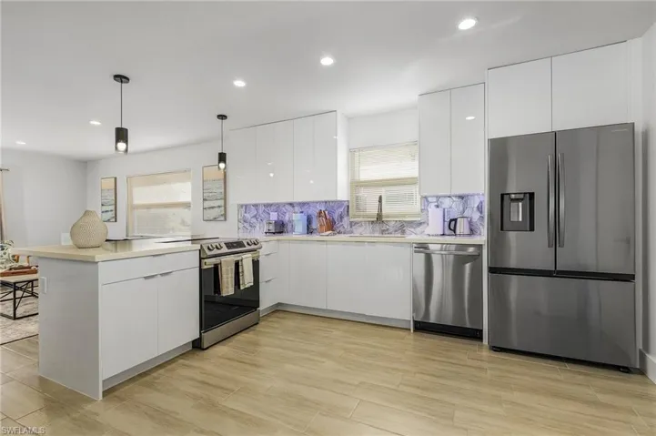 Kitchen with a peninsula, modern cabinets, stainless steel appliances, decorative backsplash, and white cabinets