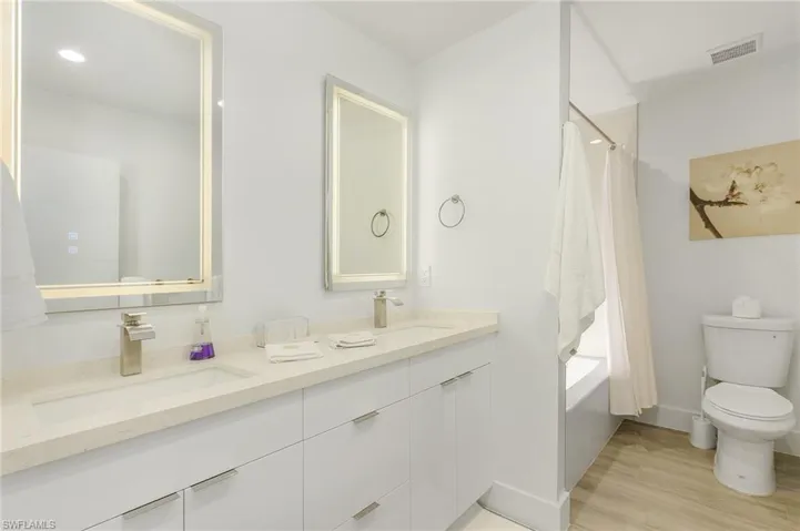 Full bathroom with shower / tub combo with curtain, double vanity, and light wood-style floors