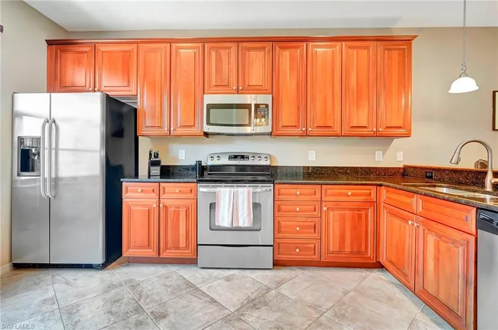 Kitchen featuring stainless steel appliances, brown cabinetry, dark stone counters, and pendant lighting