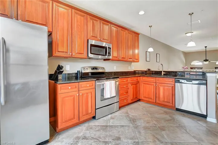 Kitchen with stainless steel appliances, brown cabinets, dark stone counters, decorative light fixtures, and a peninsula