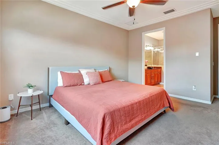 Carpeted bedroom featuring ornamental molding, ensuite bath, and ceiling fan