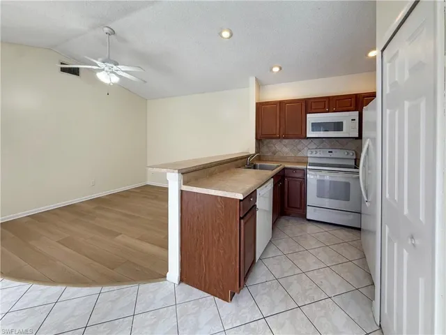 Kitchen with a peninsula, white appliances, a textured ceiling, light tile patterned flooring, and decorative backsplash