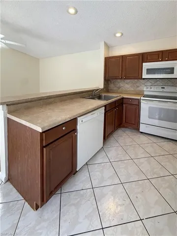Kitchen featuring white appliances, a textured ceiling, light countertops, backsplash, and a peninsula