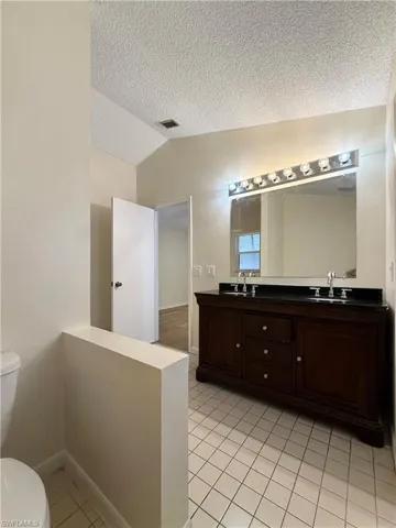 Full bathroom featuring lofted ceiling, double vanity, a textured ceiling, and light tile patterned flooring