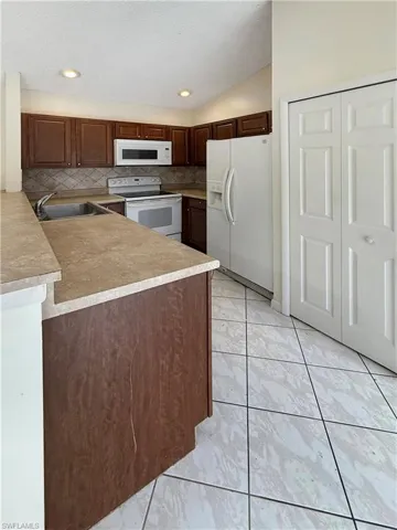 Kitchen with white appliances, light countertops, a textured ceiling, vaulted ceiling, and backsplash