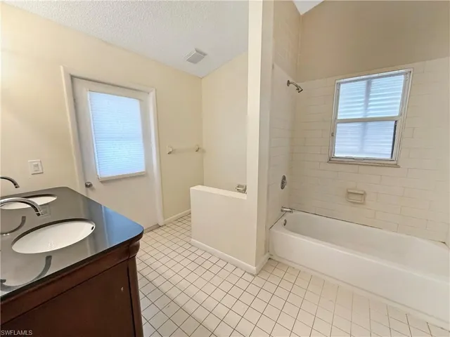 Full bathroom featuring shower / tub combination, double vanity, a textured ceiling, and light tile patterned flooring