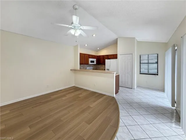 Kitchen with a peninsula, vaulted ceiling, tasteful backsplash, white appliances, and light countertops