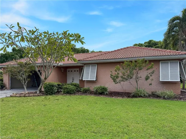 View of front facade featuring a front lawn, brick siding, a tile roof, driveway, and a garage
