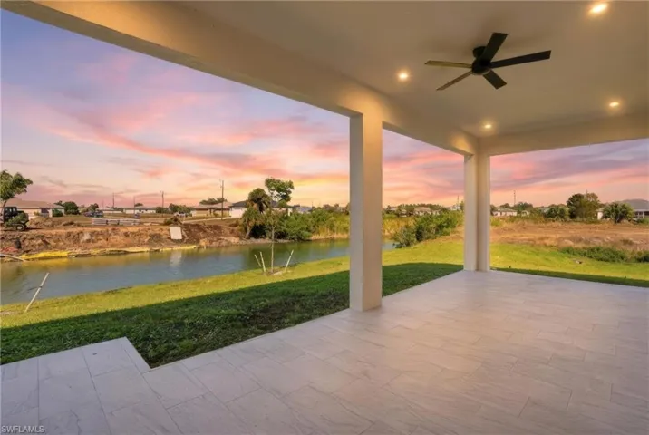 Patio terrace at dusk with ceiling fan, a patio area, a yard, and a water view