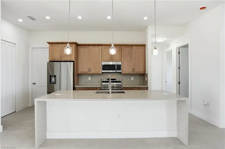 Kitchen with stainless steel appliances, light stone counters, wood finish cabinets, hanging light fixtures, and a large island