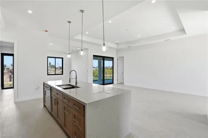 Kitchen with a tray ceiling, hanging light fixtures, light stone counters, open floor plan, and stainless steel dishwasher