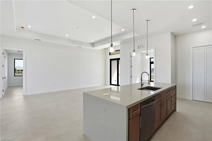 Kitchen featuring pendant lighting, light stone countertops, open floor plan, stainless steel dishwasher, and a tray ceiling