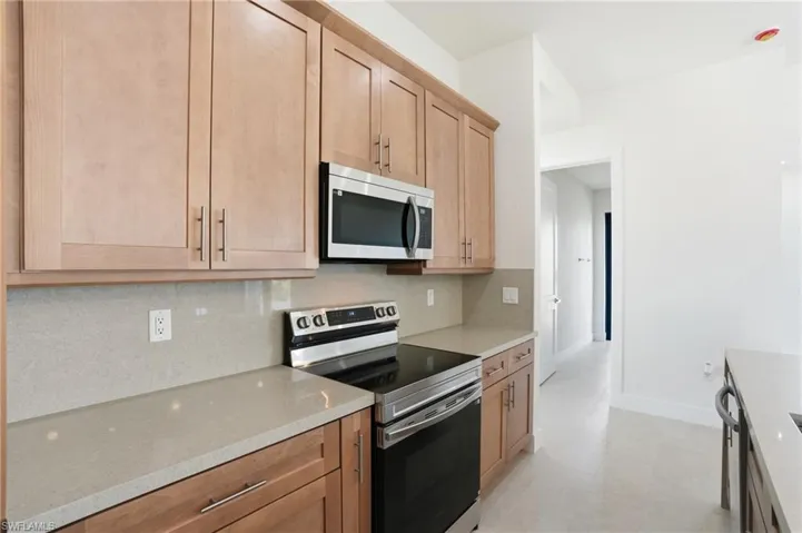 Kitchen featuring stainless steel appliances, light stone countertops, tasteful backsplash, and light wood finish cabinets