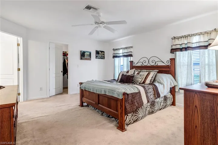 Carpeted bedroom featuring multiple windows, ceiling fan, a walk in closet, and a closet