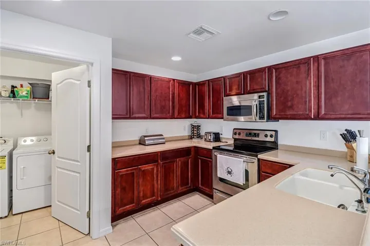 Kitchen with appliances with stainless steel finishes, independent washer and dryer, sink, and light tile patterned floors