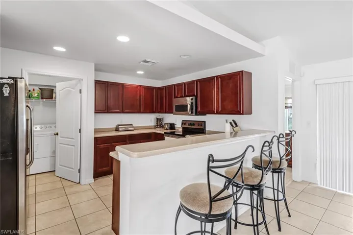 Kitchen featuring a kitchen breakfast bar, light tile patterned floors, washer / clothes dryer, stainless steel appliances, and kitchen peninsula