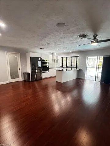 Unfurnished living room with dark wood-style floors, a textured ceiling, and a ceiling fan