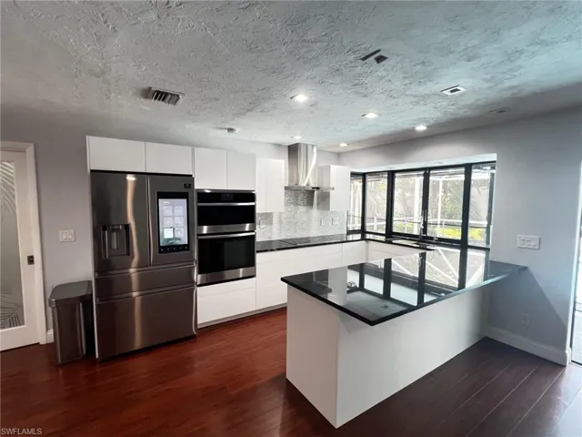 Kitchen featuring white cabinetry, stainless steel appliances, a peninsula, dark wood-type flooring, and a textured ceiling
