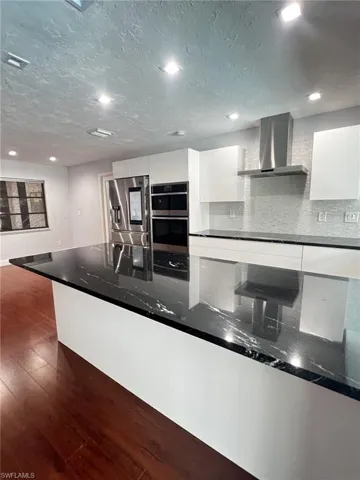 Kitchen featuring modern cabinets, white cabinets, dark stone counters, dark wood-style floors, and stainless steel appliances
