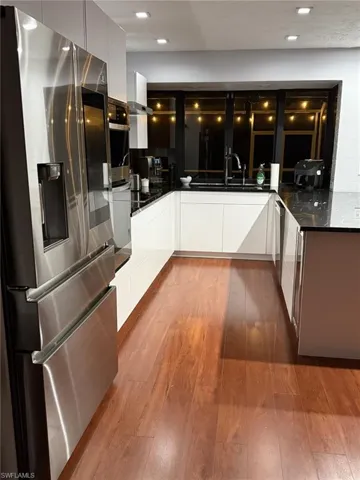 Kitchen with modern cabinets, white cabinets, stainless steel fridge with ice dispenser, dark stone countertops, and light wood-style flooring