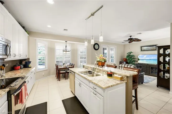 Kitchen with white cabinetry, a kitchen bar, light stone countertops, light tile patterned floors, and crown molding